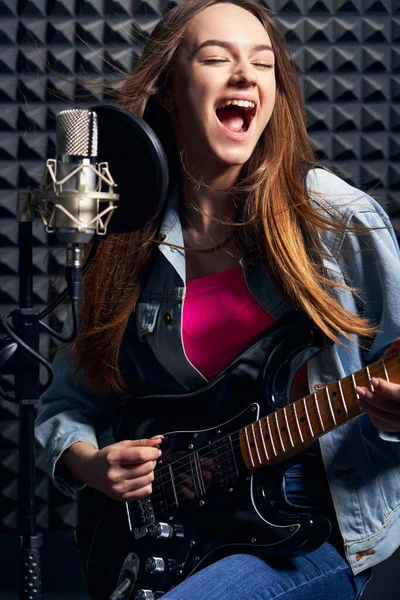 Menina músico em estúdio de gravação tocando guitarra elétrica e cantando no microfone — Fotografia de Stock