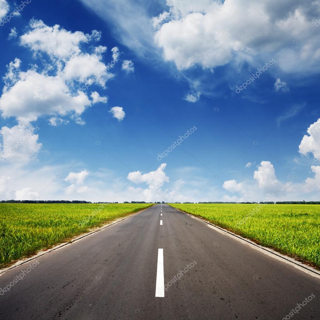 Asphalt road through the green field and clouds on blue sky in summer day