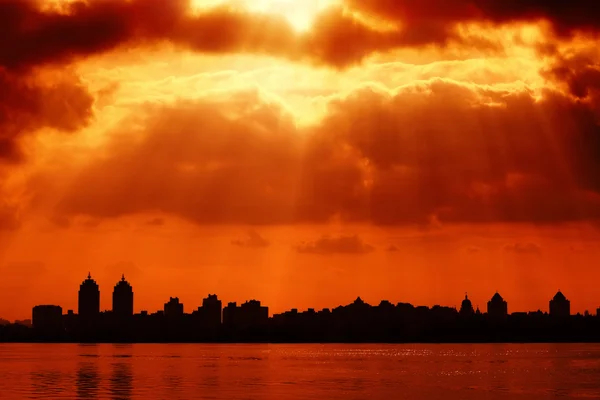 Silhouette de ville et ciel rouge avec des rayons de soleil — Photo