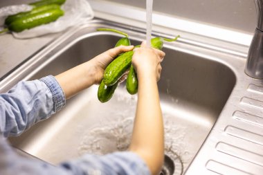 Çocukların elleri mutfakta salatalık yıkıyor.