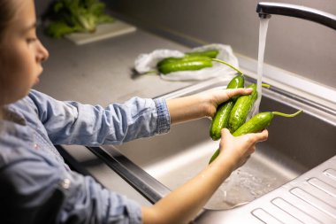 Çocukların elleri mutfakta salatalık yıkıyor.
