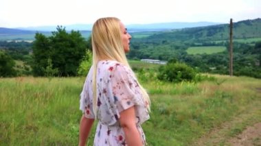 Yeşil çayırdaki yazlık elbiseli güzel kız, arkadan manzaralı..