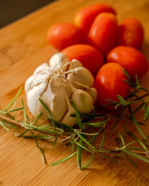 close-ups of tomatoes, rosemary and garlic on wooden board