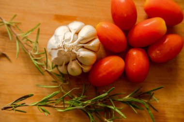 close-ups of tomatoes, rosemary and garlic on wooden board