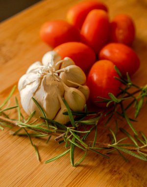 close-ups of tomatoes, rosemary and garlic on wooden board