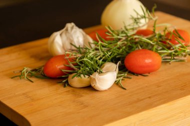 close-ups of tomatoes, rosemary and garlic on wooden board