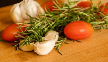 close-ups of tomatoes, rosemary and garlic on wooden board