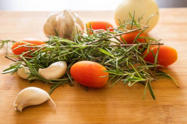close-ups of tomatoes, rosemary and garlic on wooden board