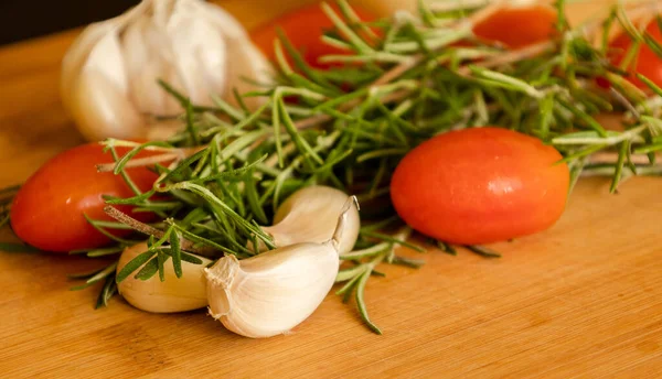 close-ups of tomatoes, rosemary and garlic on wooden board