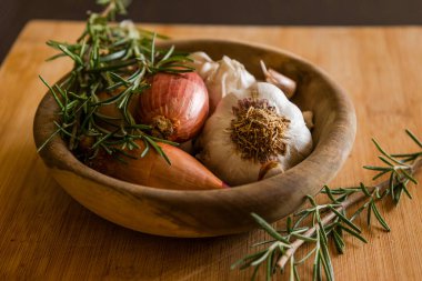 fresh raw onions, garlic, rosemary close up in wooden bowl