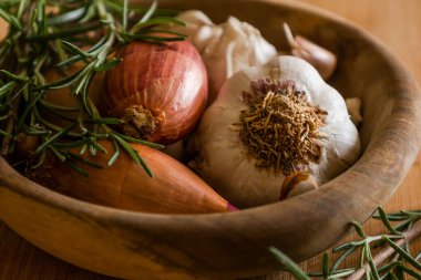 fresh raw onions, garlic, rosemary close up in wooden bowl
