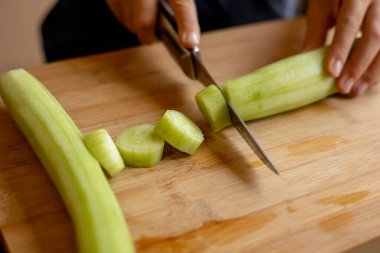 cutting cucumber at home on wooden board close up