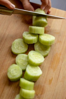 cutting cucumber at home on wooden board close up