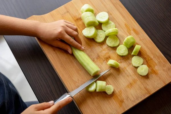 cutting cucumber at home on wooden board close up