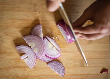 Erkek elleri kırmızı soğanı tahta tahtaya yakın kesiyor.