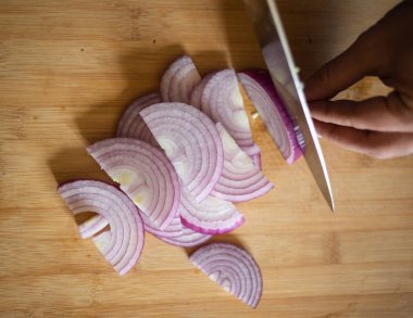 Erkek elleri kırmızı soğanı tahta tahtaya yakın kesiyor.