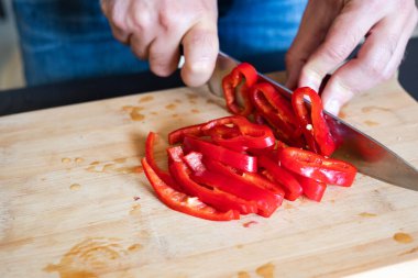 Erkek elleri kırmızı biberi tahta tahtaya yakın kesiyor.