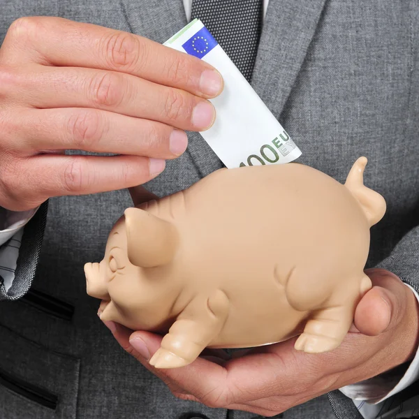 Man in pak de invoering van een euro rekening in een piggy bank — Stockfoto