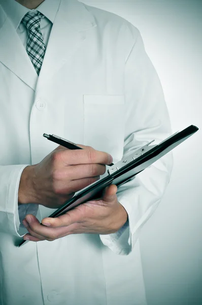 Arzt schreibt in ein Klemmbrett — Stockfoto