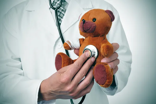 Médico auscultating um ursinho de pelúcia com ligaduras na cabeça e um — Fotografia de Stock