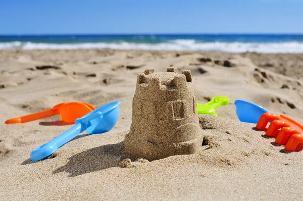 Castelo de areia e pás de brinquedo na areia de uma praia — Fotografia de Stock