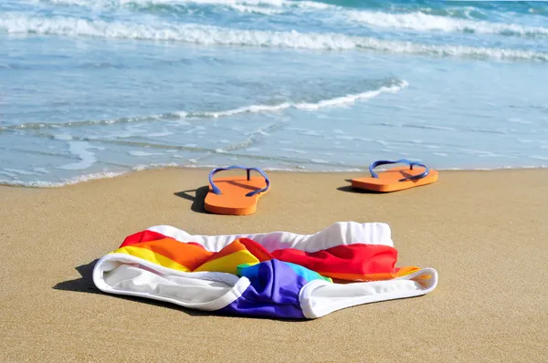 Rainbow swimsuit and flip-flops in the sand of a beach — Stock Photo, Image