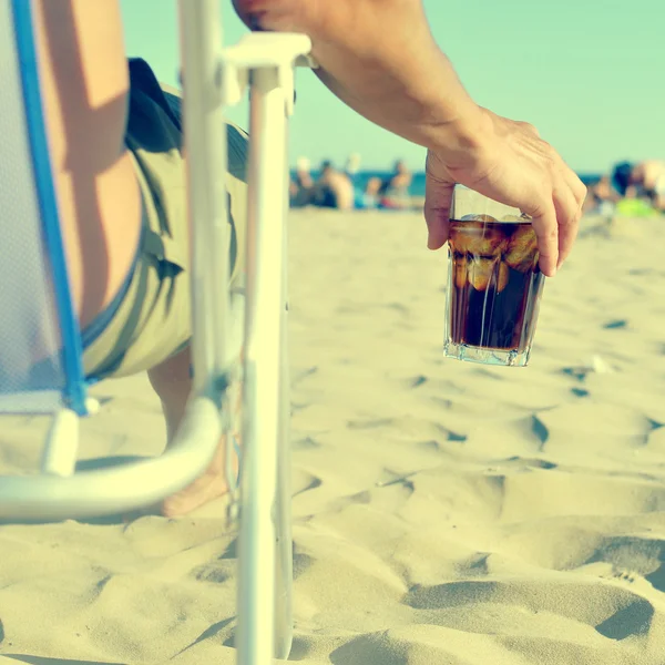 Mladý muž se sklem s cola nápoj na pláži, s filt — Stock fotografie