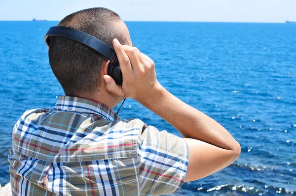 Genç adam denizin önünde kulaklık ile müzik dinlemek — Stok fotoğraf