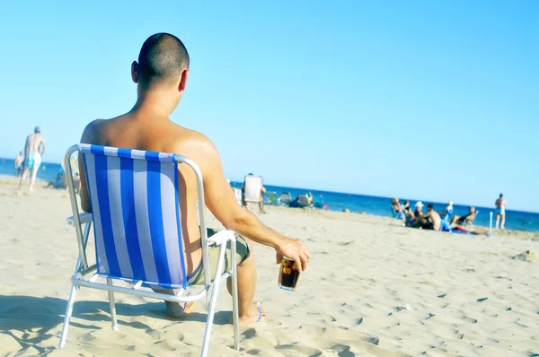 Jonge man opknoping op het strand, met een glas met cola drinken — Stockfoto