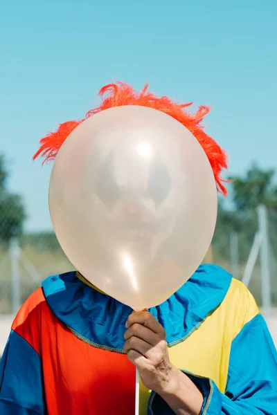 一个毛骨悚然的小丑的特写 身穿五颜六色的黄色 红色和蓝色服装 手持气球站在他面前 — 图库照片