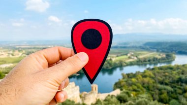 the hand of a man with a red marker pointing the old town of Miravet, Spain, built next to the Ebro River, with the Serra de Cardo and Els Ports mountain range in the background clipart