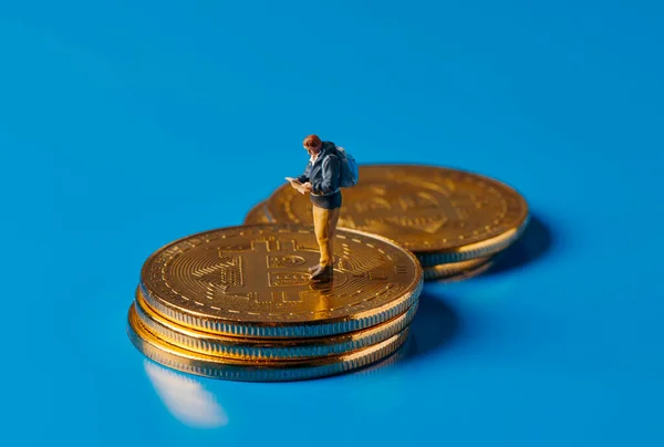 一个微型冒险家的特写镜头 他在蓝色背景的一堆比特币上看到了一幅地图 描绘了投资于这种虚拟货币的冒险性质 — 图库照片