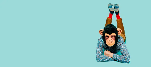 猿のマスクをした男は青い背景の上に横になっていて左側に空白のスペースがありウェブバナーやヘッダーとして使用するパノラマ形式で — ストック写真