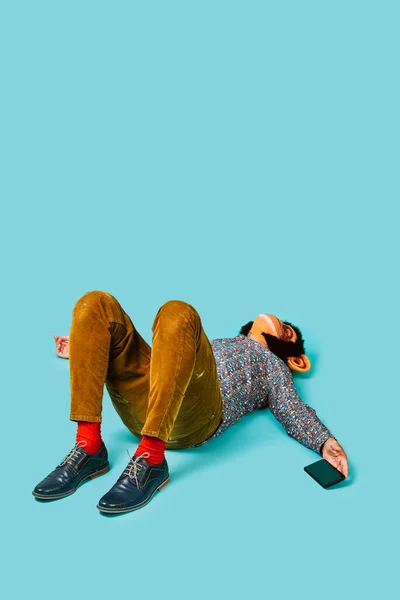 一个戴着猴子面具 手里拿着智能手机的年轻人躺在蓝色的背景上 上面有一些空白的地方 — 图库照片