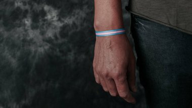 a young person wears a wristband patterned with a transgender pride flag on a gray background, in a panoramic format to use as web banner or heade clipart