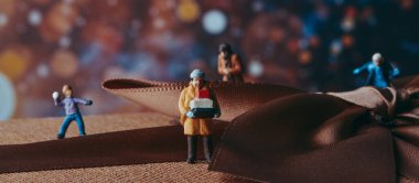 Minyatür bir adam, palto giyiyor, bir yığın kutu taşıyor, hediye kutusunda, yanında bir çocuk kartopu atıyor ve diğer bazı minyatür insanlar, panoramik formatta web pankartı veya başlık olarak kullanılıyor.