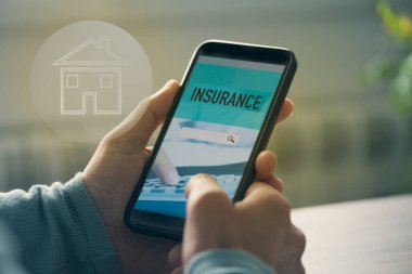 Oturma odasındaki bir masada oturan, akıllı telefonuyla ev sigortasını arayan, simüle edilmiş arama motoru olan genç bir beyaz adamın yakın çekimi.