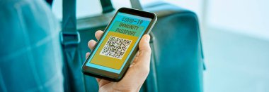 Genç bir iş adamı, havaalanının bekleme salonunda akıllı telefonunun ekranında simüle edilmiş elektronik covid-19 dokunulmazlık pasaportuyla panoramik bir formatta web pankartı ya da başlık olarak kullanılacak.