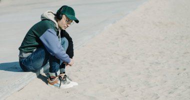 Yakışıklı, orta yaşlı bir adam, modern gündelik giysiler giyiyordu. Güneşli bir kış gününde şehir kumsalının yanında, gezinti alanında oturan bir çift kulaklık kullanarak müzik dinliyordu.