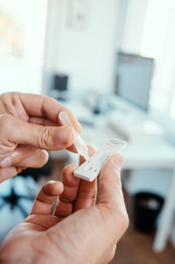 Ofiste genç bir Kafkasyalı 'nın kendi örneğini seri antijen test cihazına yerleştirirken yakın plan görüntüsü.