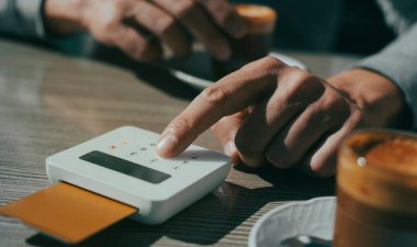 Kaldırımdaki bir kafede oturan genç bir adamın yakın plan fotoğrafı. Kredi kartının şifresini kablosuz ödeme terminalinin şifresine ekliyor.