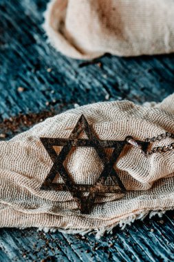 David 'in yıldızı şeklindeki eski ve paslı bir kolyeye yakın, yırtık pırtık bir kumaş parçasında, gri, ahşap bir yüzey üzerinde.