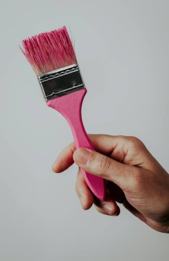 Soluk gri bir arkaplanda pembe bir boyayla boya fırçası tutan bir adamın yakın çekimi.