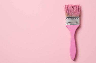 Pembe boyalı pembe bir fırçanın yüksek açılı görüntüsü solda biraz boşluk olan soluk pembe bir arka planda.