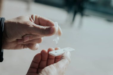 Sokakta genç bir adamın yakın plan görüntüsü. Kendi örneğini covid-19 antijen test cihazına yerleştiriyor.