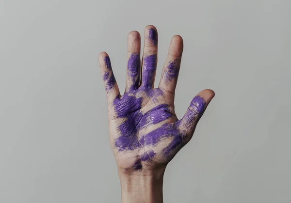 一个男子举起的手的特写 他的手掌上有一些紫色油漆的污迹 背景是苍白的灰色 — 图库照片