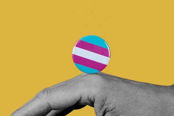 一个黑白相间的年轻高加索人的手部特写 带着一个别针按钮 其图案是黄底的跨性别自豪旗 — 图库照片