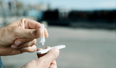 Sokaktaki genç bir adam, kendi numunesini web pankartı olarak kullanmak üzere panoramik formatta test cihazına koyarak kendi kendini covid-19 antijen testi yapıyor.