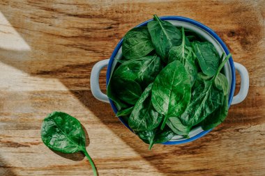 Tahta bir masaya yerleştirilmiş beyaz bir diş minesi tenceresinde taze ıspanak yapraklarının yüksek açılı görüntüsü.