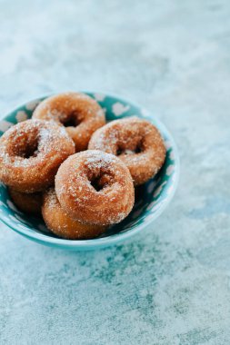 Üzerinde ev yapımı rosquillas bulunan mavi bir seramik kaseye yakın plan. Taştan bir yüzeye serpiştirilmiş tipik İspanyol çörekleri.